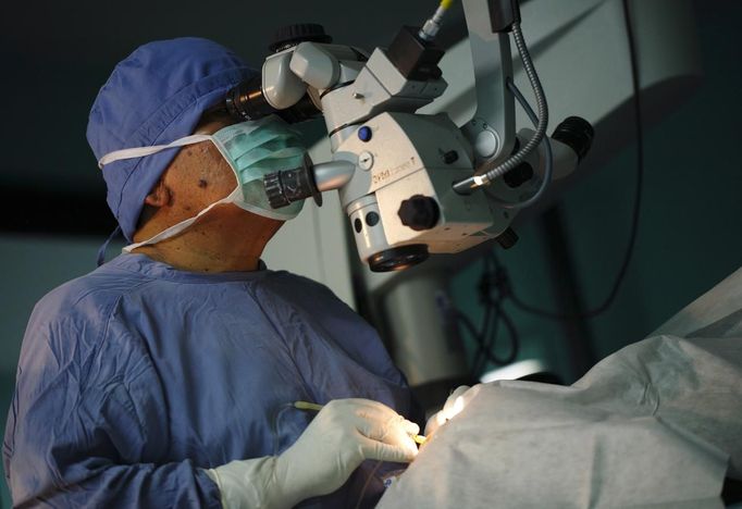 Surgeon Sanduk Ruit looks into the eyes of a patient through a microscope while conducting an operation to remove cataracts at the Tilganga Eye Center in Kathmandu April 25, 2012. A simple eye operation pioneered by Ruit, a Nepali national, at the Tilganga Eye Centre has benefited tens of thousands of people in Nepal and other countries in Asia and Africa, where surgical teams from the centre provide much needed care in field camps. Picture taken April 25, 2012. REUTERS/Navesh Chitrakar (NEPAL - Tags: HEALTH SOCIETY POVERTY) Published: Kvě. 2, 2012, 4:44 dop.