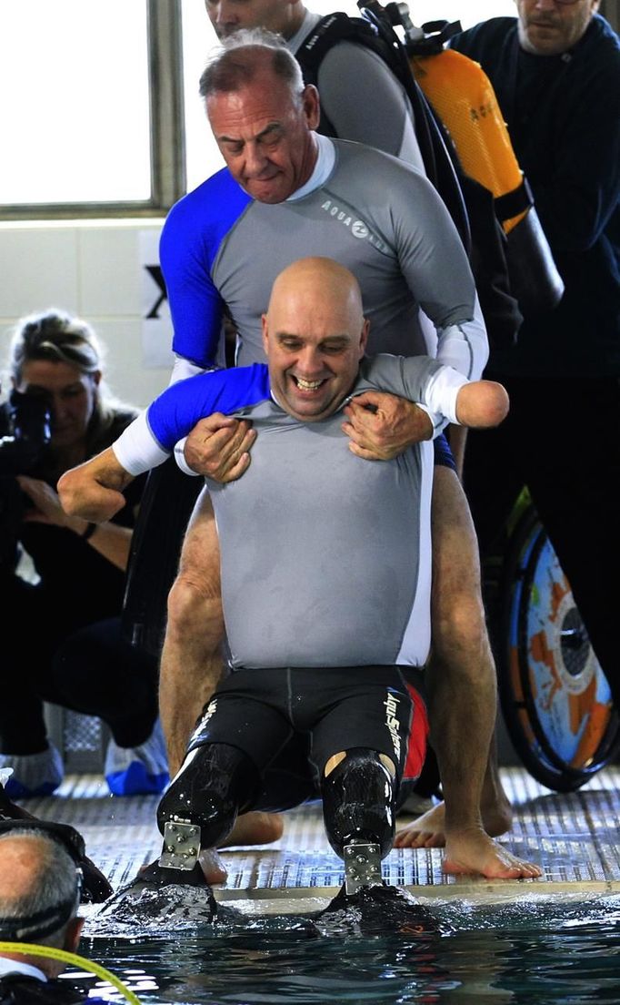 French athlete Philippe Croizon (C), whose arms and legs were amputated after an electric shock accident in March 1994, is helped by an unidentified diver to enter a 33 metre (36 yard) deep pool, the world's deepest pool built to train professional divers, at Nemo33 diving centre in Brussels January 10, 2013. Croizon, who swam with adapted prostheses that had flippers attached, broke a world record and became the first disabled person to dive to 33 metres, according to the organisers. REUTERS/Yves Herman (BELGIUM - Tags: SOCIETY SPORT DIVING) Published: Led. 10, 2013, 4:36 odp.