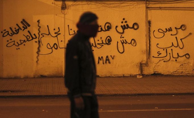 A protester, who opposes Egyptian President Mohamed Mursi, walks during clashes with riot police in front of the presidential palace in Cairo February 11, 2013. Protesters demanding the departure of Egyptian President Mohamed Mursi clashed with police outside his palace on Monday on the second anniversary of the overthrow of veteran autocrat Hosni Mubarak. The graffiti reads, "Police are thugs , Mursi dog of Mubarak." REUTERS/Amr Abdallah Dalsh (EGYPT - Tags: POLITICS CIVIL UNREST) Published: Úno. 11, 2013, 11:59 odp.