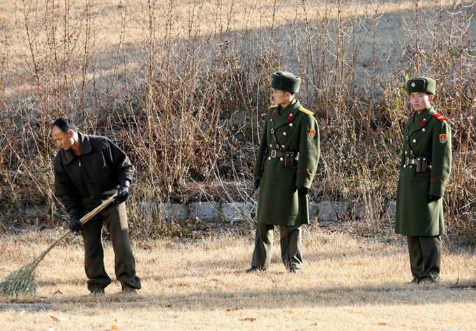 Vojáci hlídají pracujícího civilistu. Má za úkol ukldit demilitarizované pásmo mezi Korejemi od listí.