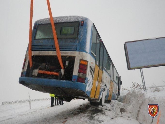 Vyprošťovací vozidlo Bizon vyzvedlo pomocí hydraulického ramene a vázacího popruhu na silnici zadní část autobusu na silnici.