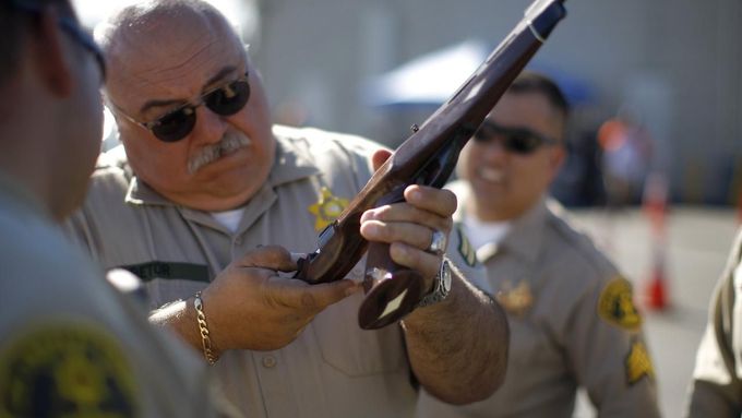A Los Angeles County Sheriff's deputy takes in guns from motorists trading them in at the 'Gifts for Guns' gun buyback in Compton, California, January 21, 2013. People can trade in their guns anonymously and with no questions asked in exchange for $200 gift cards for assault weapons, $100 gift cards for shotguns, handguns and rifles, and $50 for non-operational firearms. U.S. President Barack Obama is pushing to address controversial issues surrounding gun violence and regulation as he begins his second term in office. REUTERS/David McNew (UNITED STATES - Tags: POLITICS SOCIETY) Published: Led. 21, 2013, 10:45 odp.