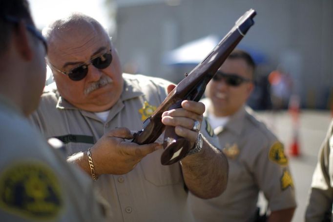 A Los Angeles County Sheriff's deputy takes in guns from motorists trading them in at the 'Gifts for Guns' gun buyback in Compton, California, January 21, 2013. People can trade in their guns anonymously and with no questions asked in exchange for $200 gift cards for assault weapons, $100 gift cards for shotguns, handguns and rifles, and $50 for non-operational firearms. U.S. President Barack Obama is pushing to address controversial issues surrounding gun violence and regulation as he begins his second term in office. REUTERS/David McNew (UNITED STATES - Tags: POLITICS SOCIETY) Published: Led. 21, 2013, 10:45 odp.