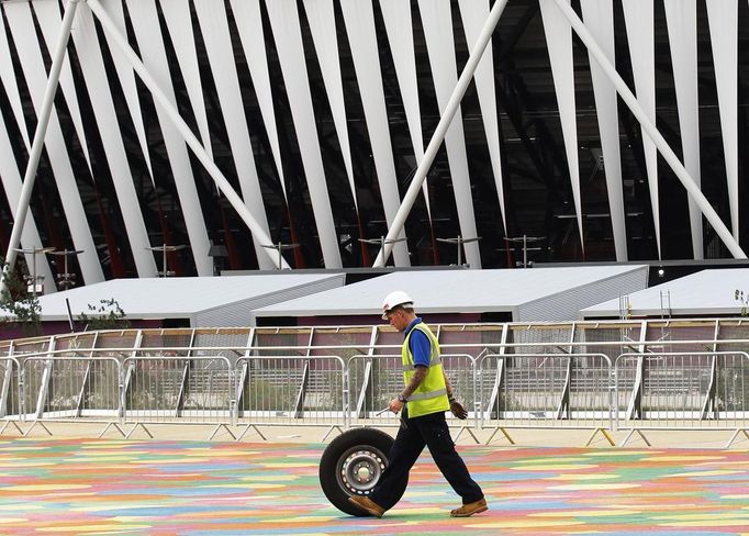 A worker pushes a tyre past the Olympic Stadium in the London 2012 Olympic Park at Stratford in London July 17, 2012. REUTERS/Luke MacGregor (BRITAIN - Tags: SPORT OLYMPICS TPX IMAGES OF THE DAY) Published: Čec. 17, 2012, 12:11 odp.