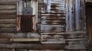 Patchwork of rusted metal sheets covers aging wooden planks on side of traditional colonial-era Board House in Freetown