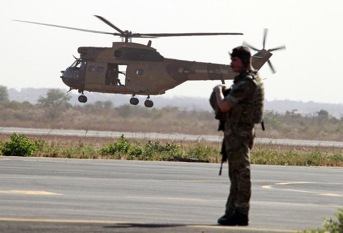 A British soldier secures the area upon the arrival of a British C17 cargo aircraft while a French Puma helicopter takes off at the Mali air force base near Bamako January 18, 2013. The British Royal Air Force is lending logistical support to France as it sends forces to Mali. REUTERS/Eric Gaillard (MALI - Tags: CIVIL UNREST CONFLICT MILITARY) Published: Led. 18, 2013, 6:17 odp.