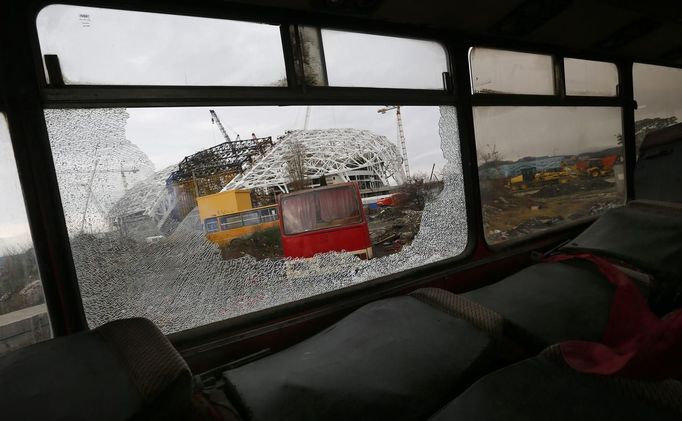 The Olympic stadium for the Sochi 2014 Winter Olympics is seen through the broken window of a scraped bus within the perimeter of the Olympic Park in Adler, near Sochi February 18, 2013. Although many complexes and venues in the Black Sea resort of Sochi mostly resemble building sites that are still under construction, there is nothing to suggest any concern over readiness. Construction will be completed by August 2013 according to organizers. The Sochi 2014 Winter Olympics opens on February 7, 2014. REUTERS/Kai Pfaffenbach (RUSSIA - Tags: BUSINESS CONSTRUCTION ENVIRONMENT SPORT OLYMPICS) Published: Úno. 18, 2013, 5:58 odp.