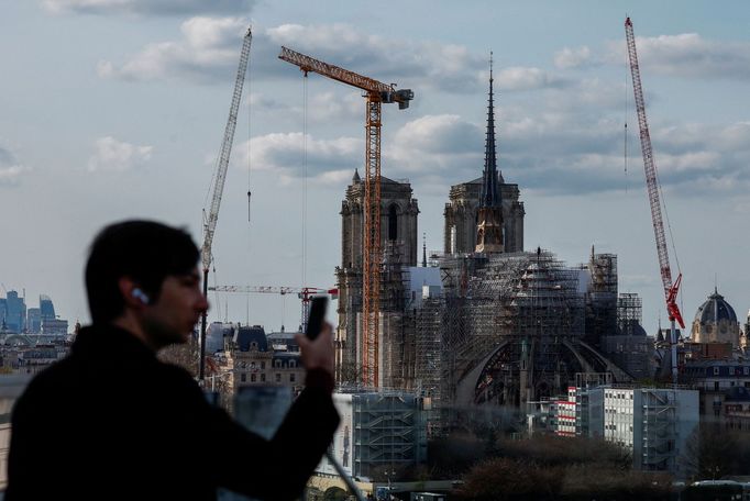 A man takes pictures near the spire, surmounted by a rooster and a cross, of the Notre-Dame de Paris Cathedral, which was ravaged by a fire in 2019, as restoration works