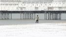 A man walks along the snow covered beach next to Brighton Pier in Brighton, southern England March 12, 2013. Southern England was hit with heavy snow overnight. REUTERS/Luke MacGregor (BRITAIN - Tags: ENVIRONMENT SOCIETY) Published: Bře. 12, 2013, 1:19 odp.