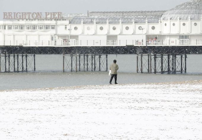 A man walks along the snow covered beach next to Brighton Pier in Brighton, southern England March 12, 2013. Southern England was hit with heavy snow overnight. REUTERS/Luke MacGregor (BRITAIN - Tags: ENVIRONMENT SOCIETY) Published: Bře. 12, 2013, 1:19 odp.