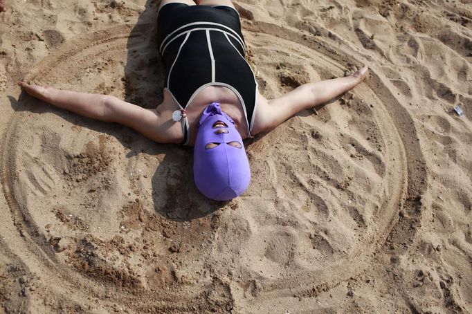 A woman, wearing a nylon mask, creates a circle in the sand as she lies down during her visit to a beach in Qingdao, Shandong province July 6, 2012. The mask, which was invented by a woman about seven years ago, is used to block the sun's rays. The mask is under mass production and is on sale at local swimwear stores. REUTERS/Aly Song (CHINA - Tags: SOCIETY ENVIRONMENT TRAVEL) Published: Čec. 6, 2012, 4:30 odp.