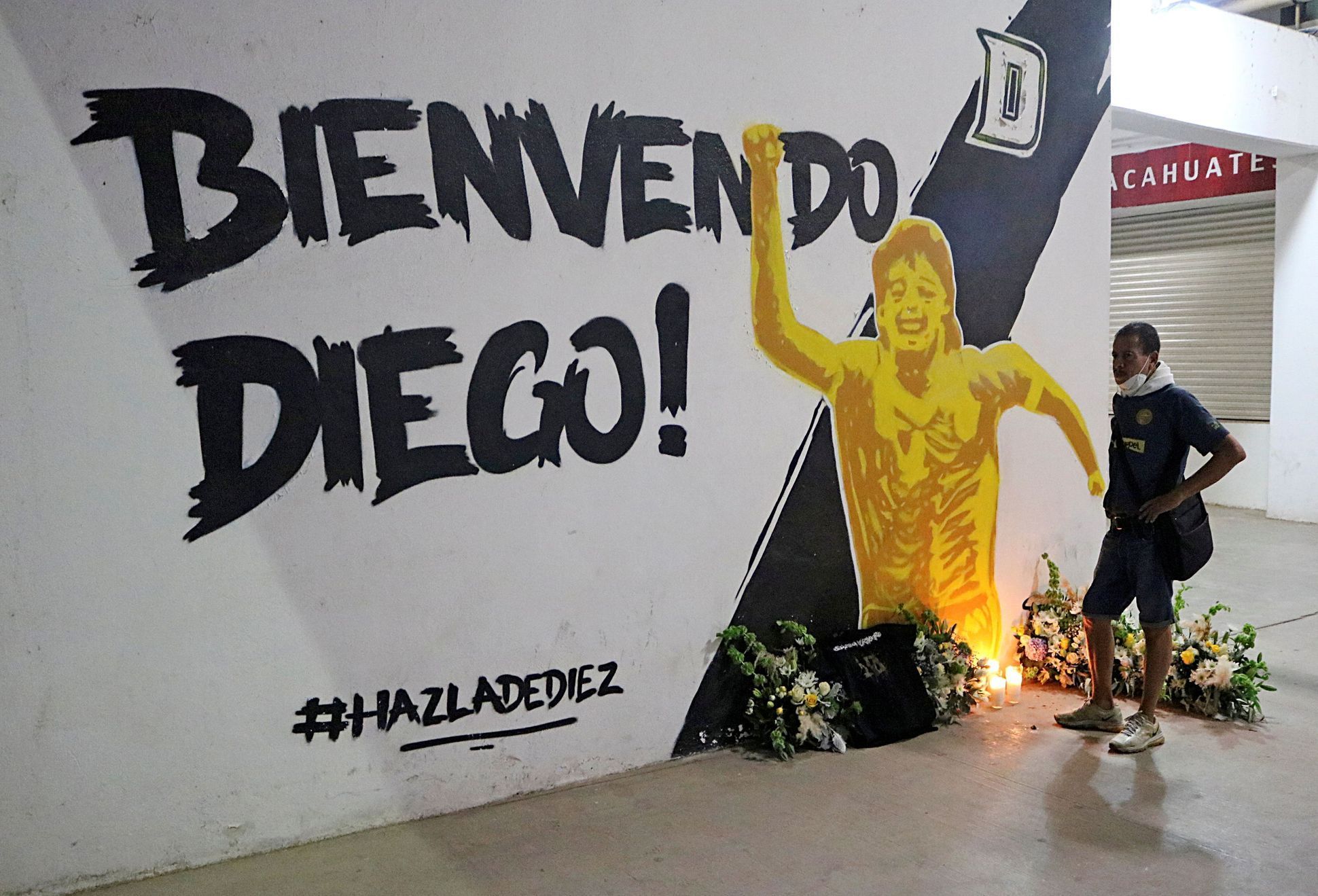 A man stands next to a mural showing late Argentine soccer legend Maradona at the Dorados stadium in Culiacan