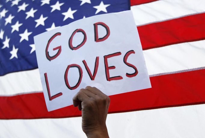 A man holds a sign during a vigil for victims behind the theater where a gunman opened fire on moviegoers in Aurora, Colorado July 22, 2012. Residents of a Denver suburb mourned their dead on Sunday from a shooting rampage by a "demonic" gunman who killed 12 people and wounded 58 after opening fire at a cinema showing the new Batman movie. President Barack Obama headed to Aurora, Colorado, on Sunday to meet families grieving their losses Friday's mass shooting that has stunned the nation and rekindled debate about guns and violence in America. REUTERS/Shannon Stapleton (UNITED STATES - Tags: CRIME LAW) Published: Čec. 23, 2012, 1:35 dop.