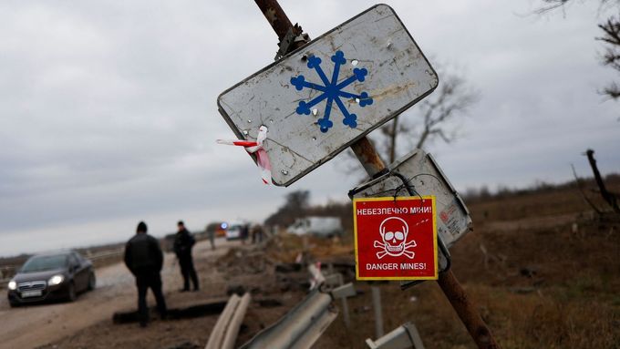 Na sloupu u hlavní silnice do Chersonu na Ukrajině je umístěna cedule s nápisem "Nebezpečí min".