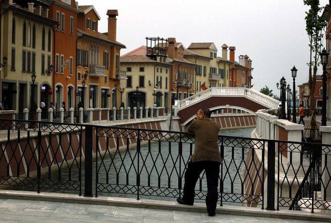 A man smokes a cigarette as he stands on a bridge over a canal that flows through the center of the Florentia Village in the district of Wuqing, located on the outskirts of the city of Tianjin June 13, 2012. The shopping center, which covers an area of some 200,000 square meters, was constructed on a former corn field at an estimated cost of US$220 million and copies old Italian-style architecture with Florentine arcades, a grand canal, bridges, and a building that resembles a Roman Coliseum. REUTERS/David Gray (CHINA - Tags: SOCIETY BUSINESS) Published: Čer. 13, 2012, 5:50 odp.