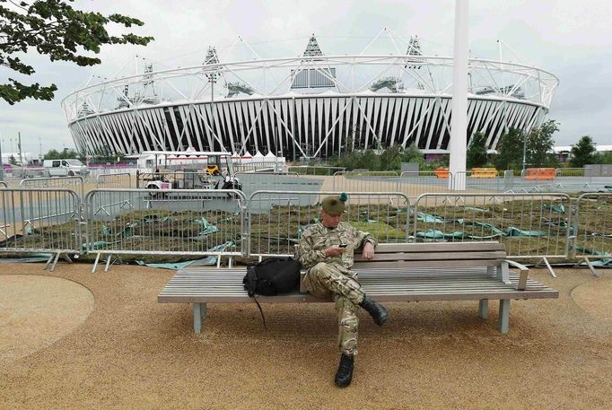 A soldier looks at his mobile phone as he sits near the Olympic Stadium at the Olympic Park in Stratford, the location of the London 2012 Olympic Games, in east London July 16, 2012. The first wave of Olympic athletes and visitors began pouring into Britain on Monday and officials played down fears that a packed London would buckle under the pressure of its biggest peacetime security and transport operation. An embarrassing shortage of security guards, fears over airport queues and questions about the capital's creaking transport system have overshadowed preparations for the Games. REUTERS/Suzanne Plunkett (BRITAIN - Tags: SPORT OLYMPICS MILITARY) Published: Čec. 16, 2012, 3:38 odp.