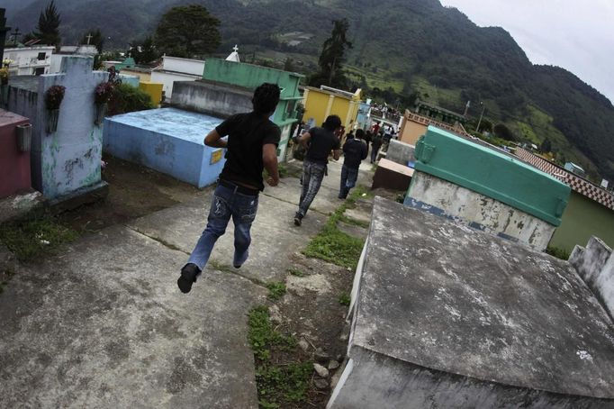 People run through a cemetery as the police rescues four men accused of theft in Tactic, in Alta Verapaz region, about 189km (117 miles) from Guatemala City, September 13, 2012. The local community tied up and beat four men who were accused of theft in the aftermath of a school killing, which had occurred on Wednesday. The man, who had entered a classroom and killed two children, ages 8 and 13, with a machete, was lynched and burnt alive by a mob, local media reported. REUTERS/Jorge Dan Lopez (GUATEMALA - Tags: CRIME LAW SOCIETY) Published: Zář. 13, 2012, 6:09 odp.