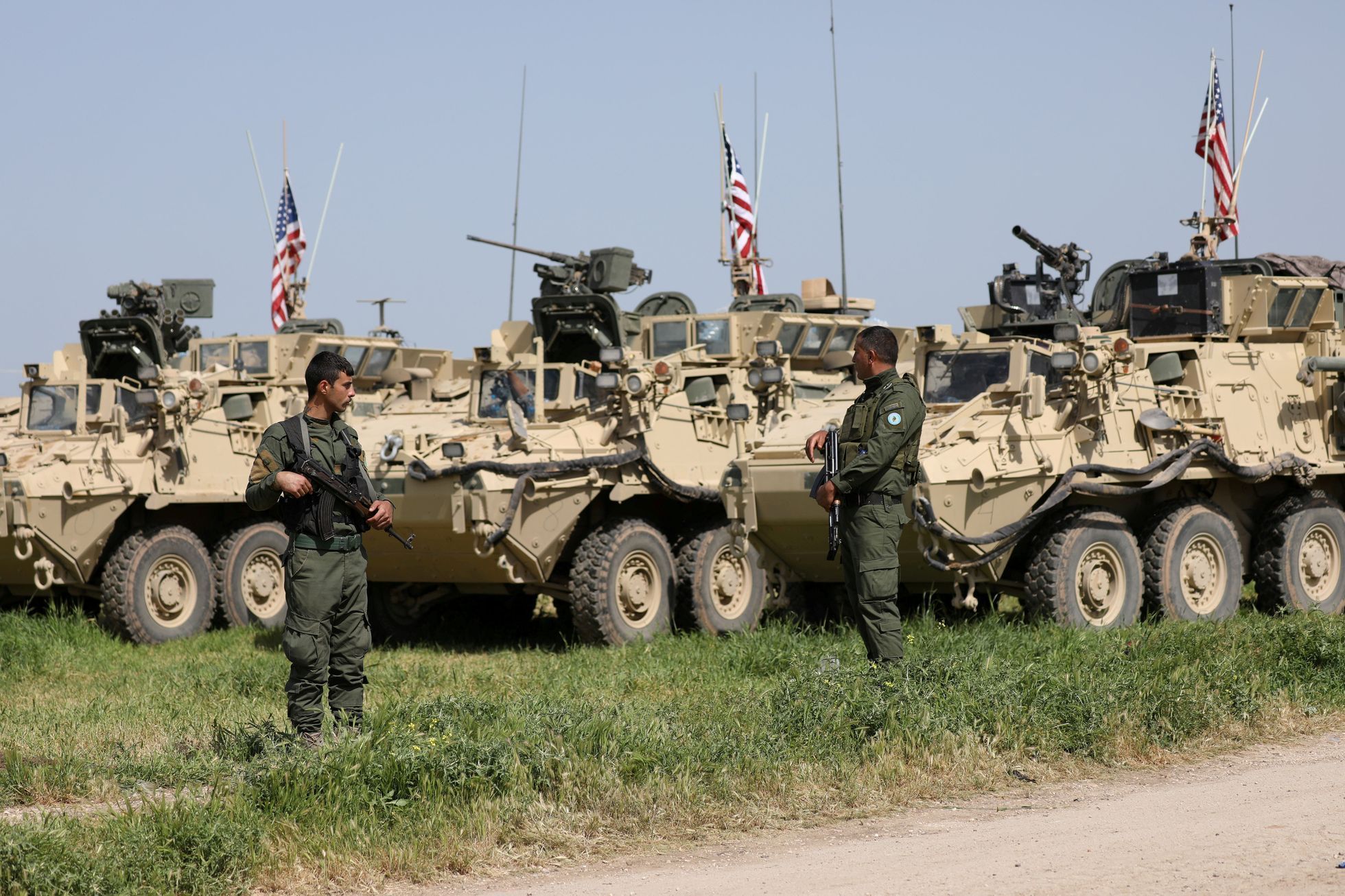 Kurdští bojovníci z YPG stojí vedle armádních vozidel USA.