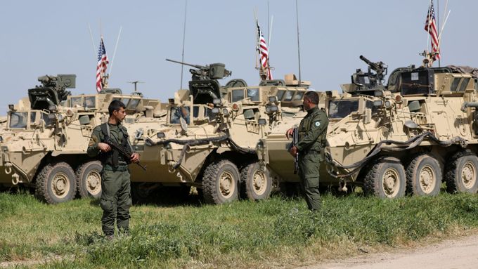 Kurdští bojovníci z YPG stojí vedle armádních vozidel USA.