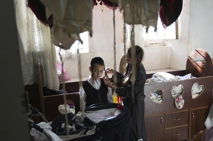 Esther Kreus (R), 13, twirls her brother's side-locks during the family's preparations for the Jewish Sabbath in Jerusalem's Mea Shearim neighbourhood June 29, 2012. The Kreus family are a member of Neturei Karta, a fringe ultra-Orthodox movement within the anti-Zionist bloc. The ultra-Orthodox Jews have gone from being a tiny minority in Israel's mostly secular society to its fastest-growing sector, now about 10 percent of the 7.8 million population. They are exempt from military duty in Israel but draft deferments and state subsidies for the ultra-Orthodox have become a divisive political issue in Israel, where the government must decide a new law by August to ensure more of them do military service. Picture taken June 29, 2012. REUTERS/Ronen Zvulun (JERUSALEM - Tags: RELIGION POLITICS MILITARY TPX IMAGES OF THE DAY) ATTENTION EDITORS - PICTURE 1 OF 21 FOR PACKAGE "ISRAEL'S ULTRA-ORTHODOX". SEARCH "ULTRA-ORTHODOX" FOR ALL PICTURES Published: Čec. 6, 2012, 9:59 dop.