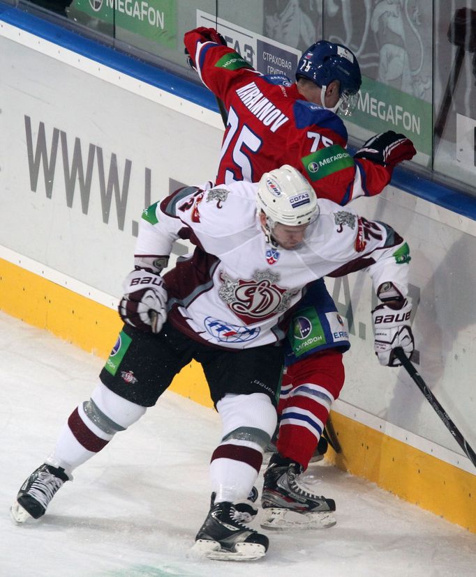 Hokejista Vitalij Karamnov (vzadu) chrání puk před Mattem Carlem v utkání KHL 2012/13 mezi Lvem Praha s Dinamem Riga .