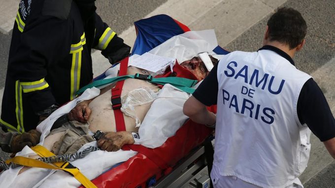 Hasič se zdravotníkem odnášejí zraněného muže z místa vlakové nehody nedaleko Paříže.