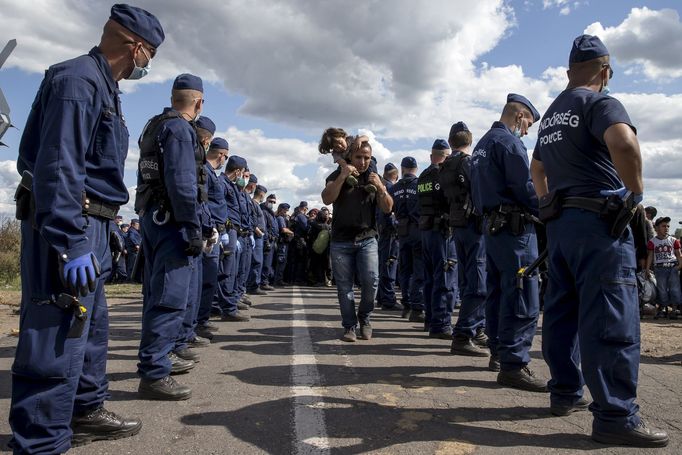 Syřan s dítětem prochází mezi maďarskými policisty poblíž uprchlického tábora Röszke.