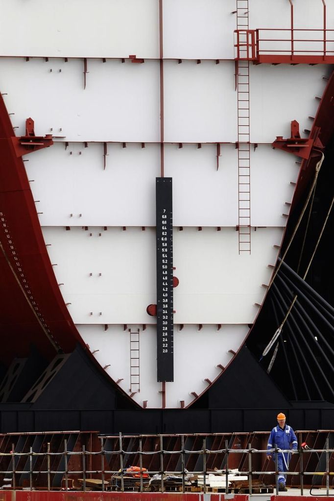 A worker walks in front of the forward section of the aircraft carrier HMS Queen Elizabeth as it is moved onto a barge at HM Naval Base in Portsmouth, southern England May 14, 2012. The hull will be transported by a sea going barge to Rosyth in Scotland where the ship will be assembled in dry dock. REUTERS/Luke MacGregor (BRITAIN - Tags: BUSINESS EMPLOYMENT MILITARY) Published: Kvě. 14, 2012, 2:54 odp.