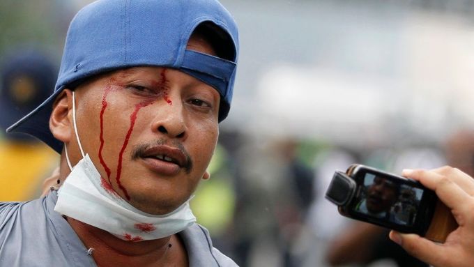 Zadržený zraněný demonstrant, kterého fotí policista