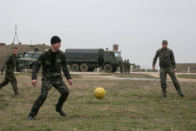 Ukrajinští vojáci hrají fotbal poblíž ruských vojenských vozidel u krymského letiště Belbek, 4. března 2014.