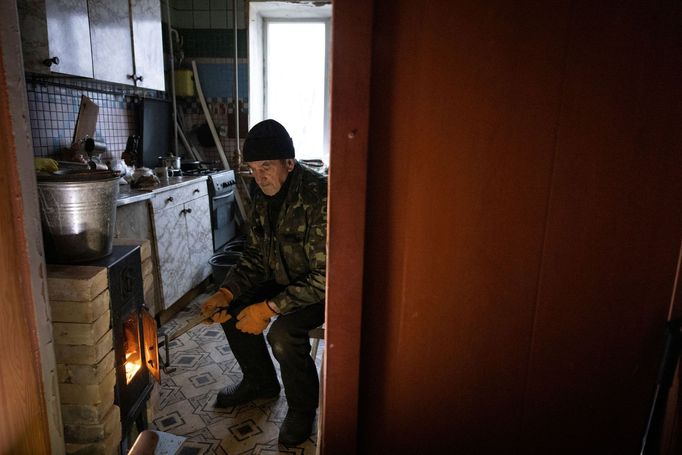 Volodymyr Tkachenko, 78, fires up a wood stove in the kitchen of his apartment that lacks central heating, water and gas in the frontline town of Lyman, amid Russia’s att