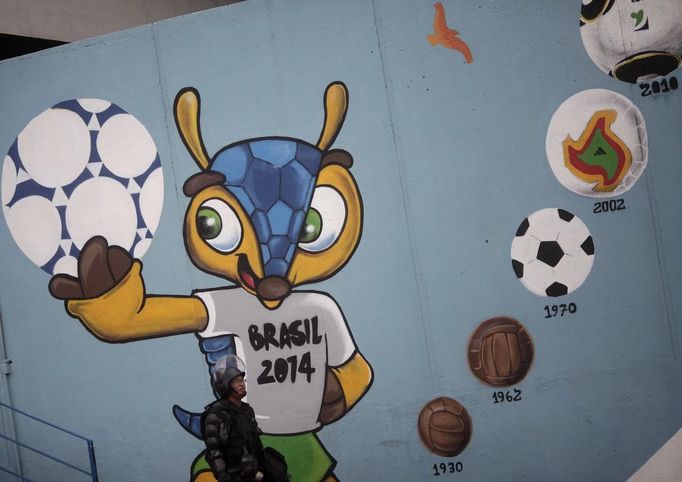 A riot policeman walks in front of a graffiti of the 2014 World Cup next to the Brazilian Indian Museum in Rio de Janeiro, March 22, 2013. Brazilian military police took position early morning outside the Indian museum, where a native Indian community of around 30 individuals who have been living in the abandoned Indian Museum since 2006. Indians were summoned to leave the museum in 72 hours by court officials since last week, local media reported. The group is fighting against the destruction of the museum, which is next to the Maracana Stadium. REUTERS/Ricardo Moraes (BRAZIL - Tags: POLITICS CIVIL UNREST) Published: Bře. 22, 2013, 5:42 odp.