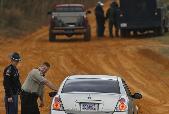 As bomb squad personnel (in back) prepare to enter the scene, law enforcement officials turn back a vehicle at a roadblock near a standoff with the shooter in Midland City, Alabama January 30, 2013. A standoff continued on Wednesday with a gunman who boarded an Alabama school bus and fatally shot the driver before fleeing with a young child and holing up in an underground bunker, authorities said. REUTERS/Phil Sears (UNITED STATES - Tags: CRIME LAW) Published: Led. 30, 2013, 7:05 odp.