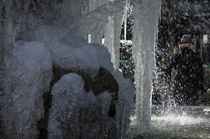 A woman takes a picture of a fountain partially covered by ice at Bryant Park in New York, January 24, 2013. Frigid arctic air held the U.S. Midwest and Northeast in its icy grip on Wednesday, with the cold so dangerous that municipal emergency warming centers opened up and ski resorts shut down. Wintry conditions from Minneapolis to Washington marked the coldest conditions in many parts of the United States in four years, but were nowhere near the record lows for January, meteorologists said. REUTERS/Eduardo Munoz (UNITED STATES - Tags: ENVIRONMENT SOCIETY) Published: Led. 24, 2013, 6:54 odp.