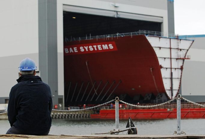 A worker watches as the forward section of the aircraft carrier HMS Queen Elizabeth is moved onto a barge at HM Naval Base in Portsmouth, southern England May 14, 2012. The hull will be transported by a sea going barge to Rosyth in Scotland where the ship will be assembled in dry dock. REUTERS/Luke MacGregor (BRITAIN - Tags: BUSINESS EMPLOYMENT MILITARY) Published: Kvě. 14, 2012, 3:39 odp.