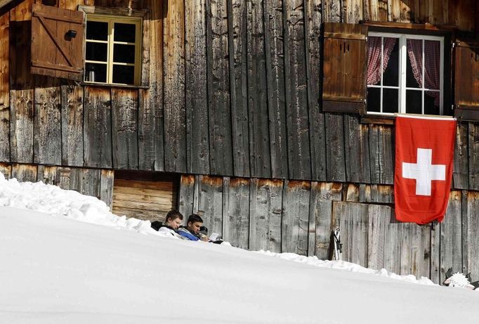 Lyžaři relaxují u alpské chalupy během slunného dne na svazích švýcarských hor, v lyžařském středisku Hoch-Ybrig.