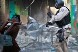 Haitský policista vyhání obuškem rabující ženu.