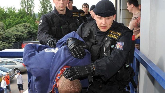 Policisté přivádějí zadrženého fanouška do improvizované soudní síně na stadionu Sparty v Praze.