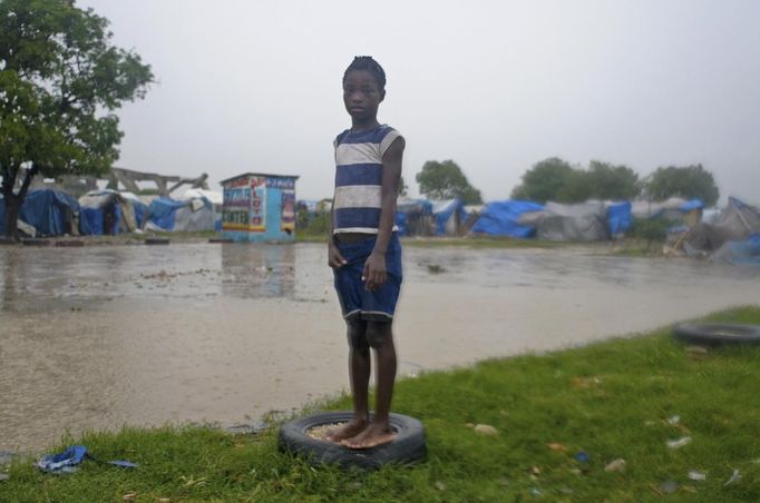 A Haitian girl stands on a tyre in a tent camp for people affected by the January 2010 earthquake, next to a street flooded by Tropical Storm Isaac in an area outside of Port-au-Prince August 25, 2012. Tropical Storm Isaac emerged over warm Caribbean waters on Saturday slightly weaker but ready to regroup after dumping torrential rains on Haiti, where thousands of people remain homeless more than two years after a devastating earthquake. REUTERS/Swoan Parker (HAITI - Tags: DISASTER ENVIRONMENT) Published: Srp. 25, 2012, 10:57 odp.