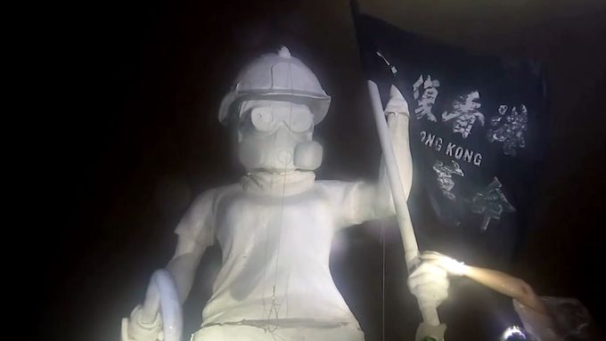 Vztyčení třímetrové figuríny s přilbou, ochrannými brýlemi a plynovou maskou na tváři.