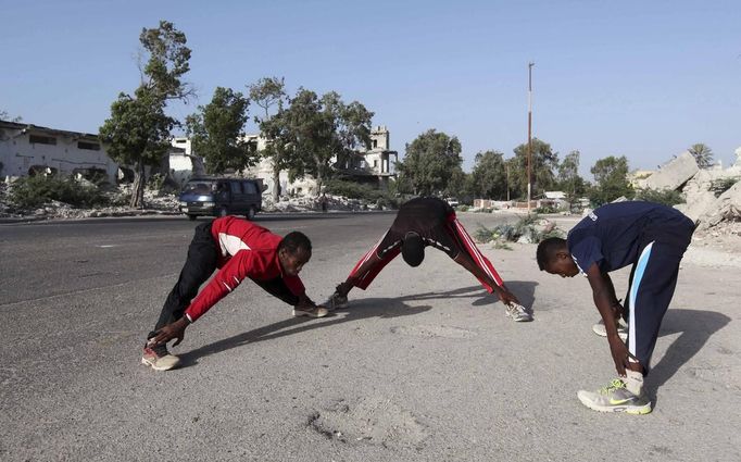 Somali athletes stretch along a street as they train during preparations for the 2012 London Olympic Games in Somalia's capital Mogadishu in this March 14, 2012 file photo. Training in a bullet-riddled stadium where the remains of a rocket propelled grenade lies discarded on the track's edge counts as progress for Somali Olympic hopeful Mohamed Hassan Mohamed. A year ago, Mogadishu's Konis stadium was a base for Islamist militants and a work out meant at times running through the streets, dodging gun-fire and mortar shells in one of the world's most dangerous cities. Picture taken March 14, 2012. To match OLY-SOMALIA-HOPES/ REUTERS/Feisal Omar/Files (SOMALIA - Tags: SPORT ATHLETICS SOCIETY OLYMPICS) Published: Čer. 11, 2012, 7:10 dop.