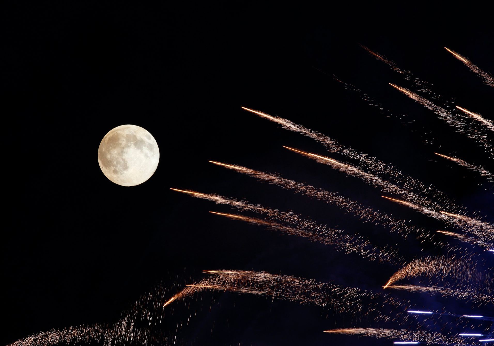 Fireworks streak past in front of the supermoon outside the town of Mosta