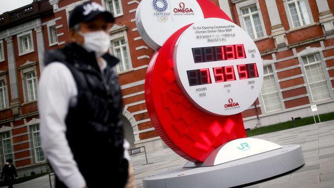 Lidé v rouškách míjí v Tokiu obří hodiny, které stále odtikávají čas, který by měl zbývat do oficiálního zahájení olympijských her (snímek je z pondělí)