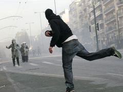 Účastník nedělní demonstrace v Athénách hází kámen na policisty. Ti museli použít vodní děla a slzný plyn
