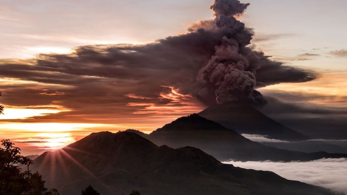 Sopka vrhla do atmosféry lávový popel, čeká se na magmatickou erupci, zatím z komína sopky vystupuje oranžová záře, čeká se, kdy se magma vylije.