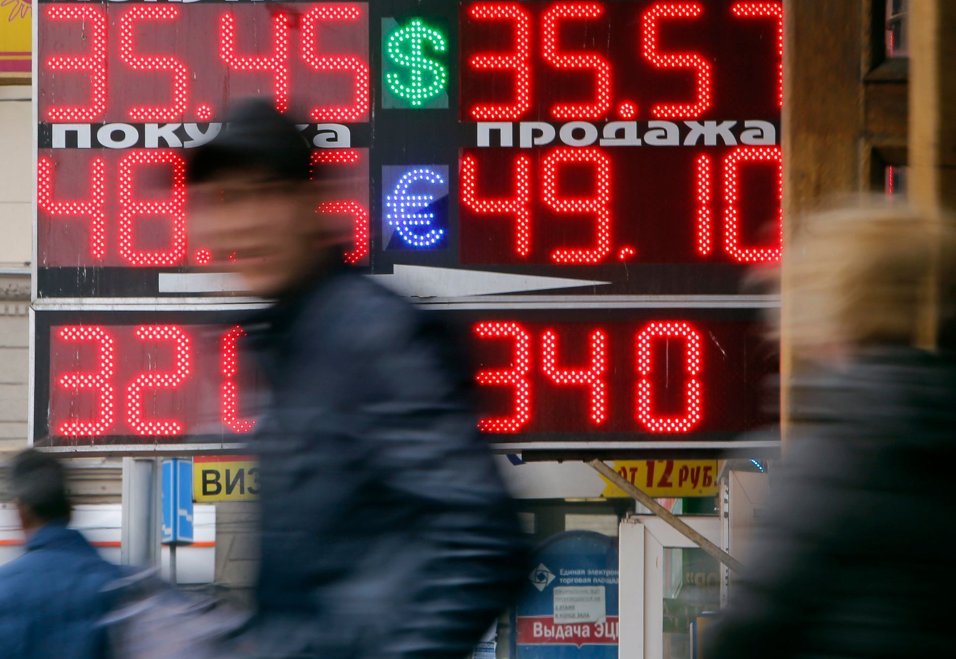 People pass by a board displaying exchange currency rates in Moscow