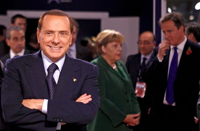 Silvio Berlusconi na summitu G20. Za jeho zády si špitá německá kancléřka Angela Merkelová s britským ministerským předsedou Davidem Cameronem.