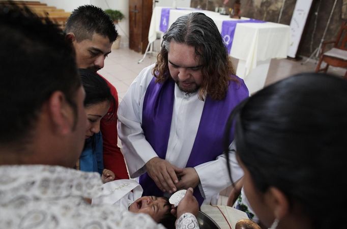 Catholic priest Adolfo Huerta (C), known as "Gofo", baptizes a young boy at the church "Our Lord of Mercy" in the El Toreo neighbourhood in Saltillo February 24, 2013. Ordained five years ago, Huerta is an unconventional priest who likes rock music, dyes the ends of his hair red, dresses in black, and enjoys riding his motorcycle. Huerta found God and priesthood while studying philosophy at the Pontifical University in Mexico City and working with HIV-positive patients and sex workers as a social activist. He says it is important to demystify faith and accept people's differences without judgment, and in his sermons he references rock songs, quotes books and tells jokes. Picture taken February 24, 2013. REUTERS/Daniel Becerril (MEXICO - Tags: RELIGION SOCIETY) ATTENTION EDITORS: PICTURE 3 OF 26 FOR PACKAGE 'CHURCH, FAITH AND ROCK'N ROLL' SEARCH 'PRIEST DANIEL' FOR ALL IMAGES Published: Bře. 15, 2013, 10:22 dop.