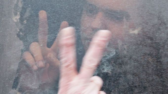 Příznivec opozice za sklem v policejním antonu. Jeho příbuzný mu zvenčí vyjadřuje podporu alespoň gestem vítězství. Snímek z Minsku 20. prosince.