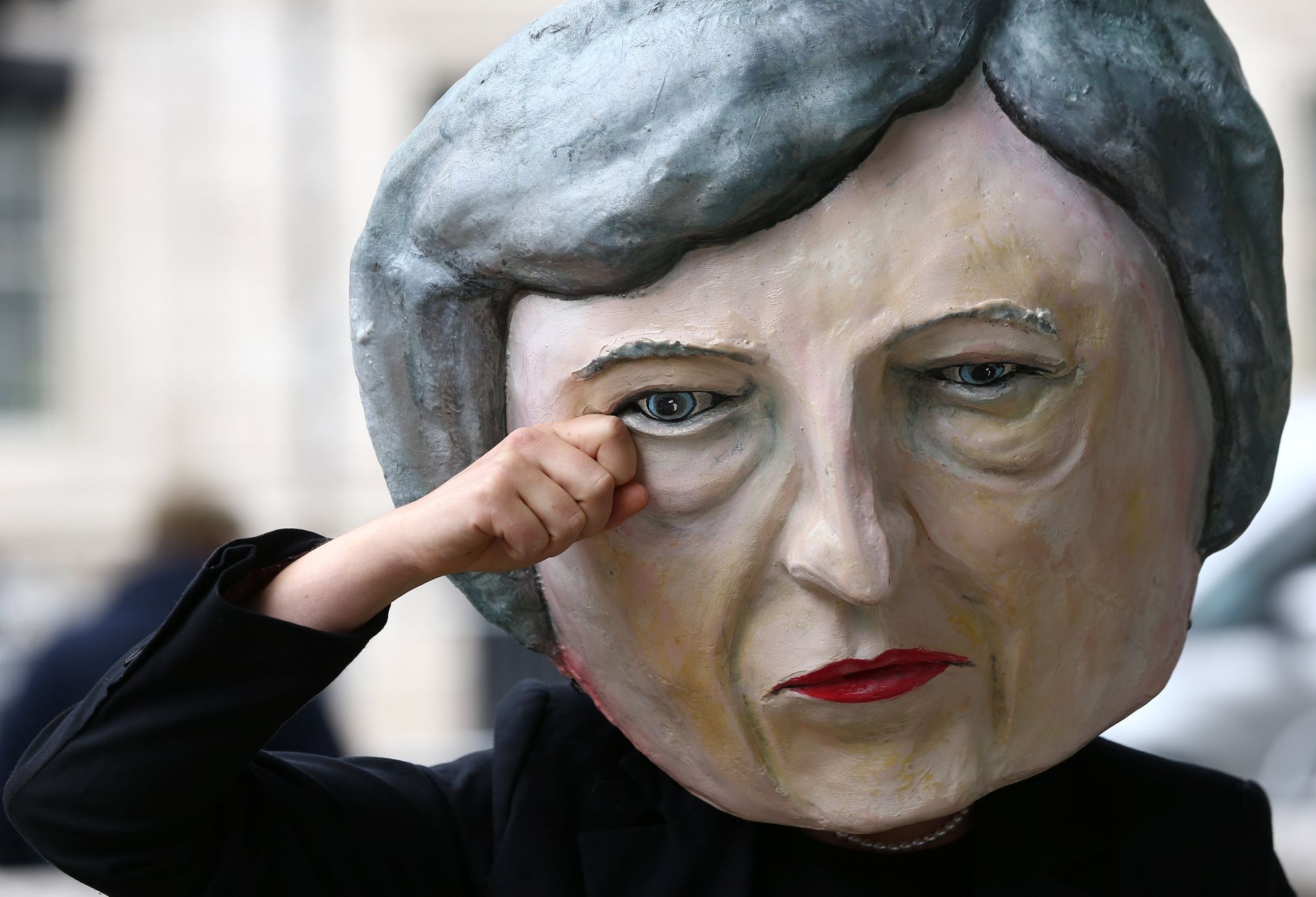 Muž s maskou Theresy Mayové stojí den po volbách před sídlem premiérky v londýnské Downing Street.